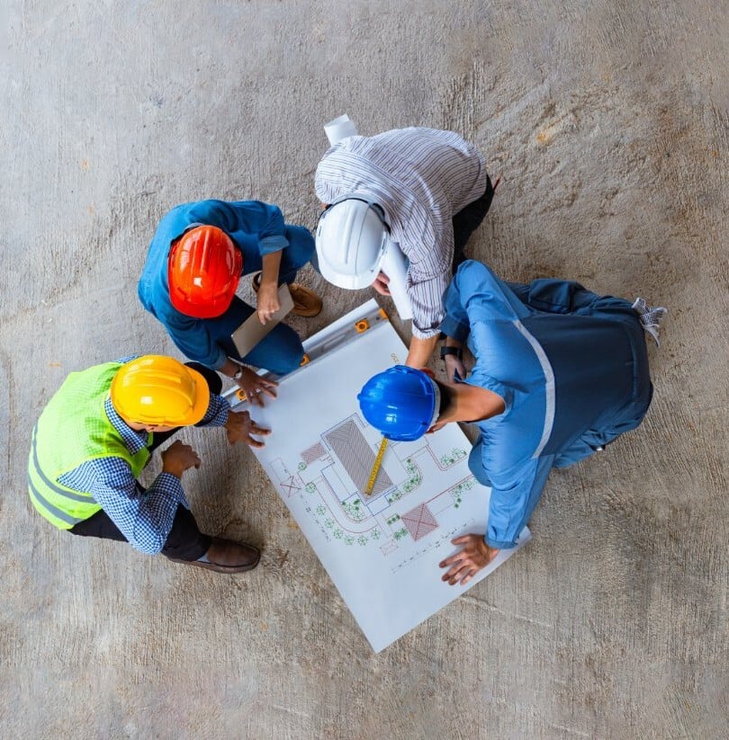 Four construction professionals in hard hats reviewing blueprints together